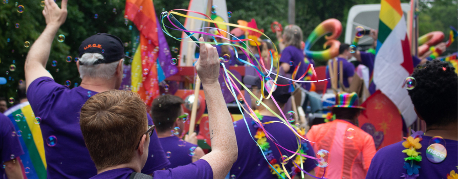 Photo taken from behind of a group marching in the Halifax Pride Parade wearing purple shirts and Pride accessories.