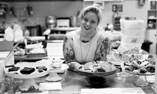 Cait Holmes standing behind a kitchen counter filled with fresh baked goods that she made for her business, Honey & Butter.