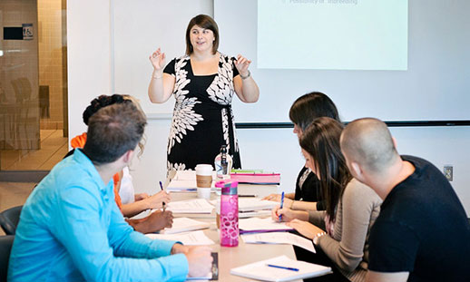 A female teacher instructing a class of men and women in a boardroom