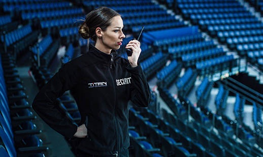 A woman in a security uniform, speaks into a walkie talkie in an empty stadium.