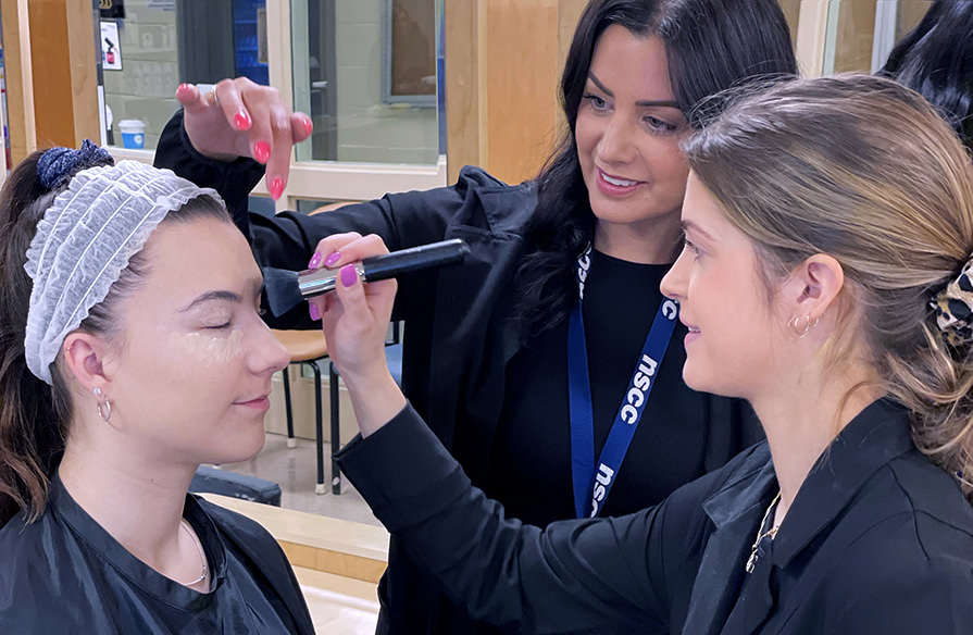 Students do makeup on someone in a salon setting. 