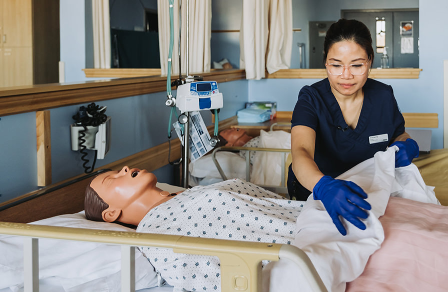 A Continuing Care student adjusts the sheets on a hospital bed working on a fake patient.