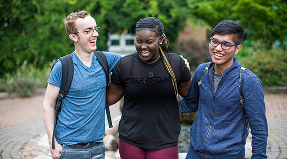 A group of 3 students walk together outdoors while smiling and laughing.