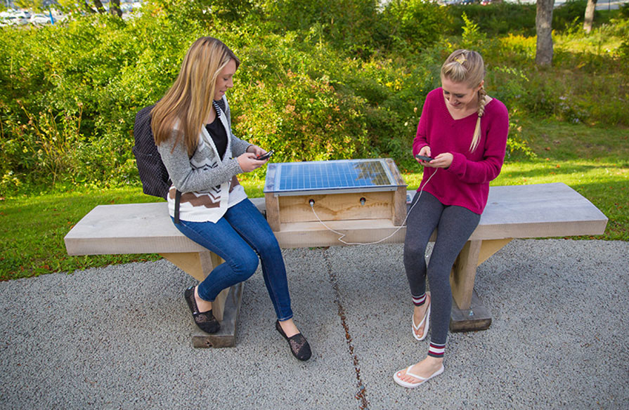 Students charging their smartphones on a solar powered bench at Ivany Campus.