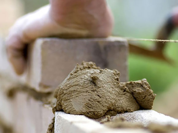 A close-up photo of hands building a wall with bricks and mortar in a brick and masonry course.