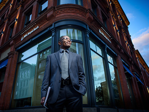 A business professional in a suit stands tall in front of a building.