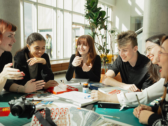 A group of students are seen sitting at a round table discussing a creative solution to their work.