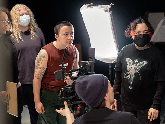 Five people stand around a camera as they work on a film set.