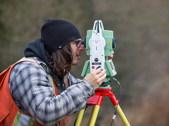 A Survey Technician student uses surveying equipment in an outdoor setting.