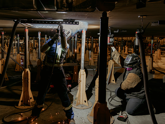 Two women graduates welding in full gear at Irving Shipyard.