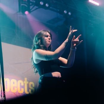 A woman providing ASL/English Interpretation on stage at a concert.
