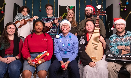 A group of people in festive holiday sweaters sitting in two rows and smile at the camera.