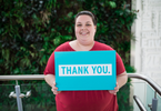 A female standing in the stairs holding a "Thank You" sign in front of the live plant wall.