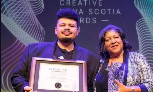 A black man and woman on stage at the Creative Nova Scotia Awards. He is holding a framed award and she is holding a physical award.