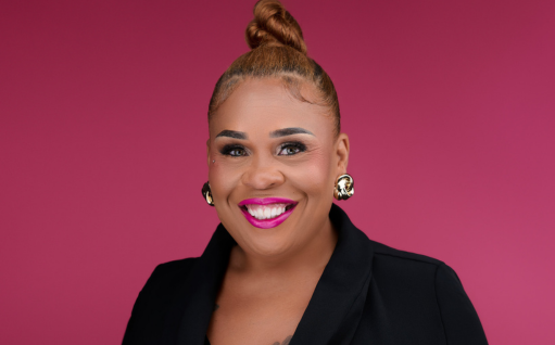 Tia Upshaw's headshot. Image is of a Black woman (Tia), wearing her hair in a bun and a black blazer. She's smiling at the camera in front of a deep pink background.