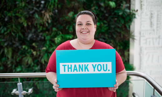 Photo of NSCC student award recipient holding aqua coloured sign saying "thank you" in white text.