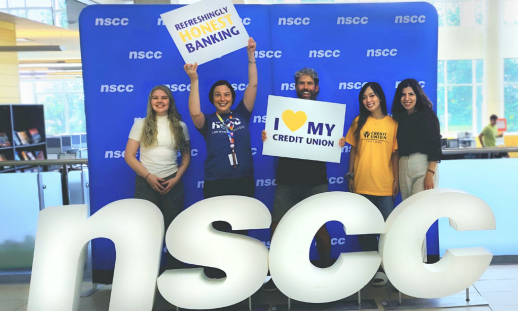 Photo of NSCC students and East Coast Credit Union staff in front of NSCC banner holding East Coast Credit Union promotional signs. 