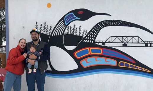 Anishinaabe artist Joshua Mangeshig Pawis-Steckley (left) poses with his partner, Maria-Margaretta, and daughter, Mino-Margaret, in front of his mural outside Mystic Loon Trading Co. in Wasauksing.