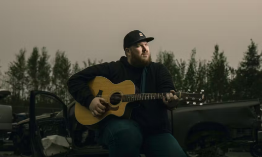 Brett Matthews' playing guitar in front of a damaged truck.