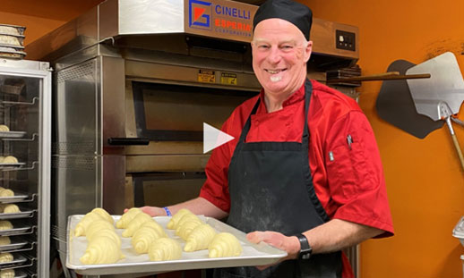 Ed Hamilton-Irving is pictured. He is working in a commercial kitchen, wearing chef's garb and holding a tray of uncooked croissants.