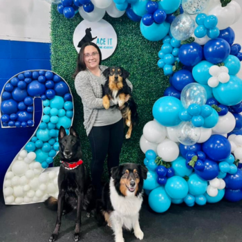 Taylor standing with her dogs in front a greenery wall pop-up with balloons during Ace It's second anniversary celebration.