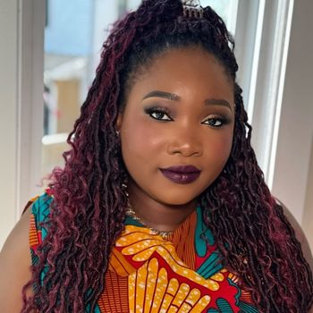 Image shows a Black woman wearing a vibrant shirt in front of a window.