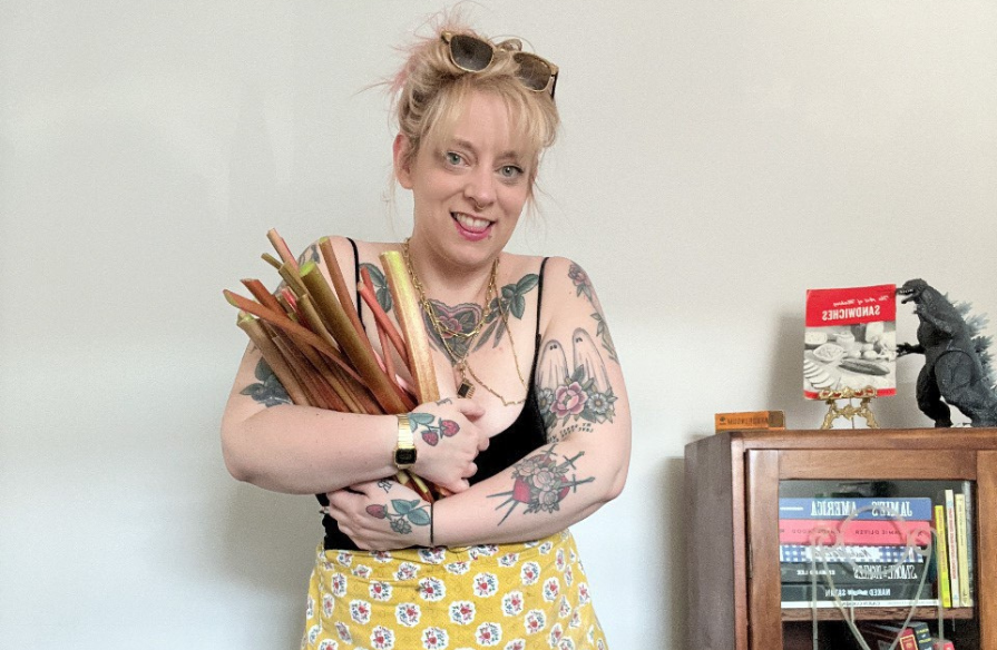 Cait Holmes with an arm full of rhubarb, standing next to a bookshelf.