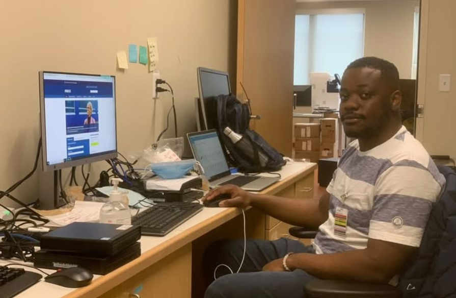 A Black man working on a computer in an office with the door open.