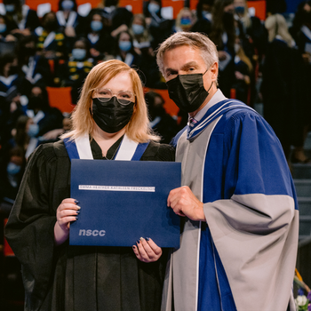 Emma Freckelton holding her diploma on stage with Don Bureaux.