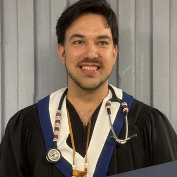Image shows an Indigenous man wearing his graduation gown, medicine pouch and stethoscope with Mi'kmaq beading.