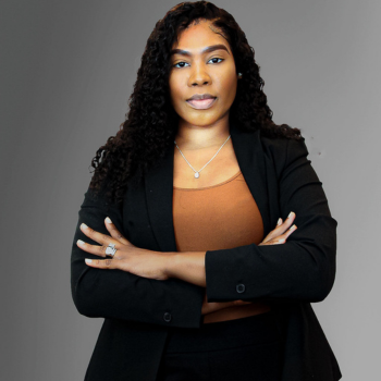 This photo is of Tamara, a Black woman who's wearing a black blazer and pants with her arms crossed with a look of determination.