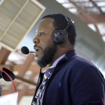 An African Nova Scotian sports broadcaster speaking into a headset at a game.