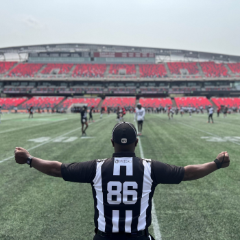 Photo taken from behind the sidelines of an African Nova Scotian officiating a football game.