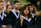 Graduating students sitting during convocation and a female student is giving the peace sign with her fingers.