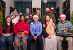A group of people in festive holiday sweaters sit in two rows and smile at the camera.