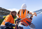 Woman and man installing solar panels in a field, both are wearing safety gear.