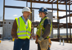 Two men wearing safety gear and talking on a construction site.