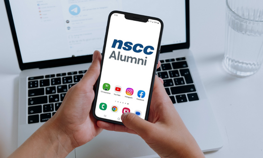 Person holding a phone that has a NSCC Alumni logo and social media icons on display.