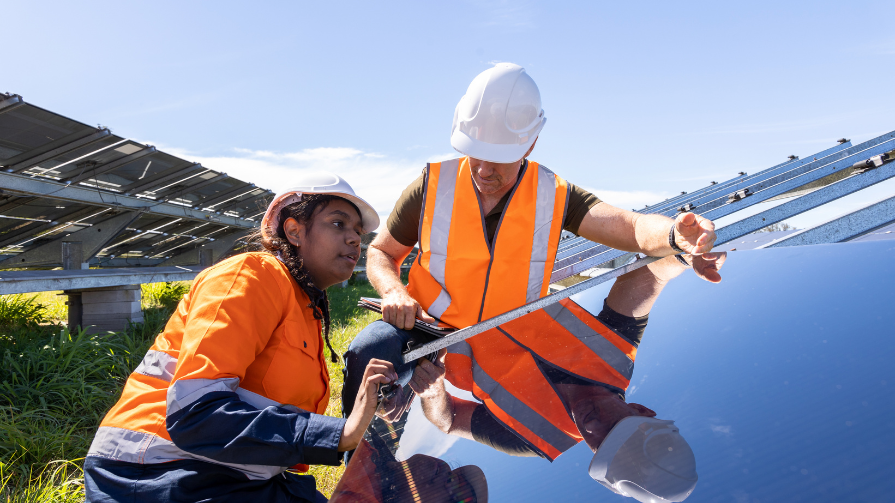 Woman and man installing solar panels in a field, both are wearing safety gear.