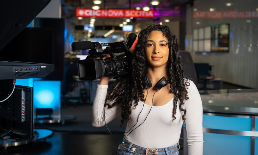 Kyah Sparks (Radio TV Journalism '15) holding a camera and gear on the set of CBC News Halifax.