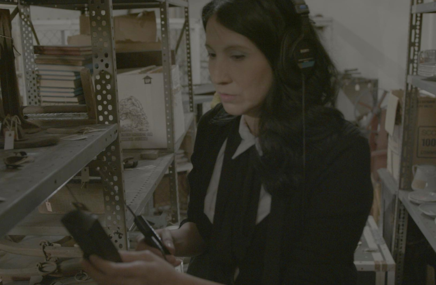 A woman in an old storage room wearing a headset and holding a recording device, trying to record ghost sounds.