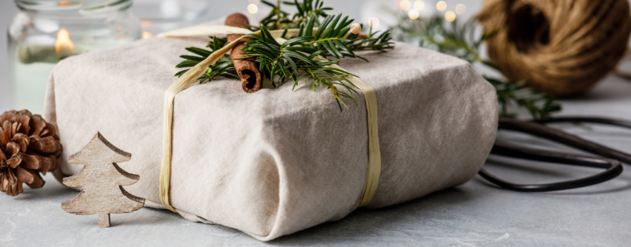 Fabric wrapped gift close up with a cinnamon stick, pine and pinecone for decoration.  