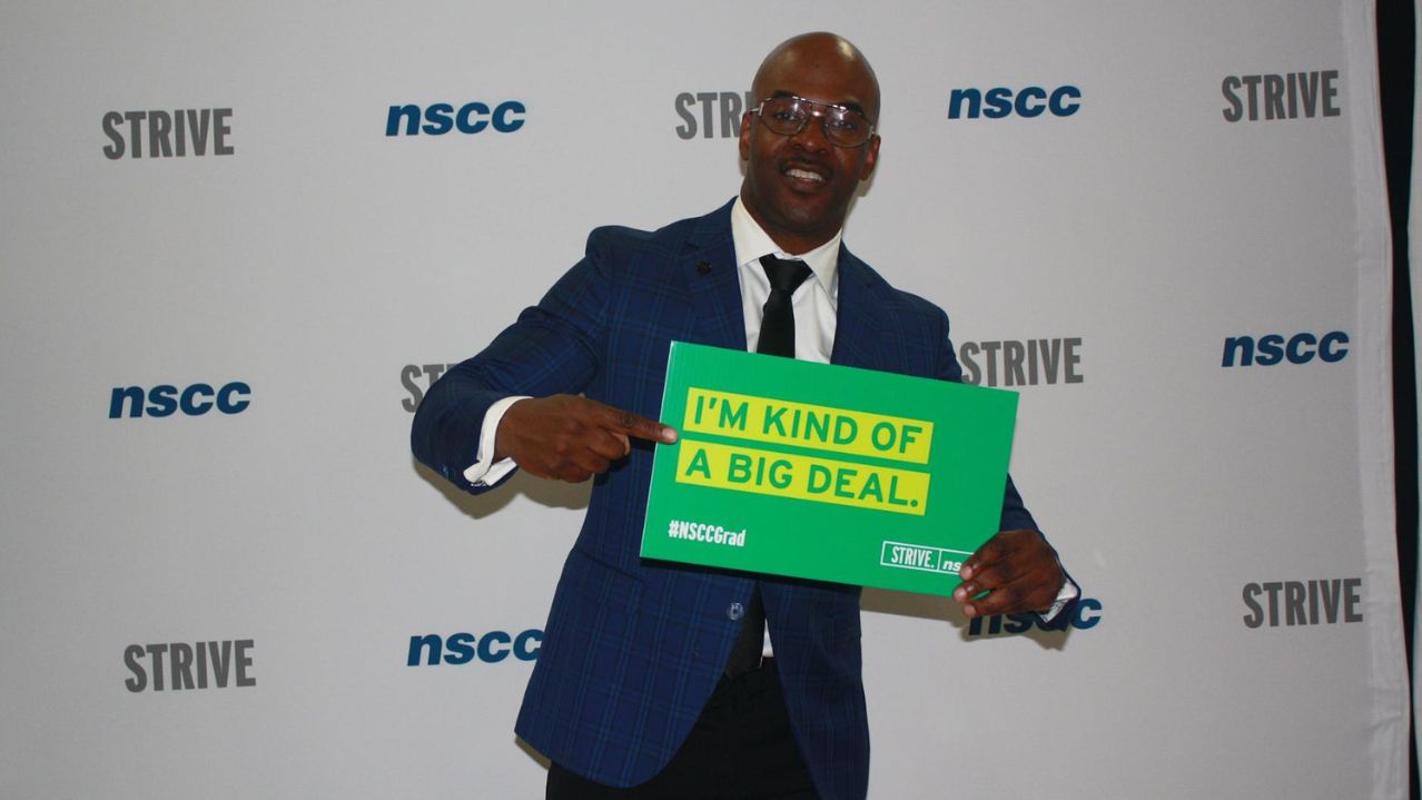 Maestro Fresh Wes holding a "I'm kind of a big deal" sign in front of an NSCC backdrop.
