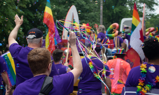 Photo taken from behind of a group marching in the Halifax Pride Parade wearing purple shirts and Pride accessories.