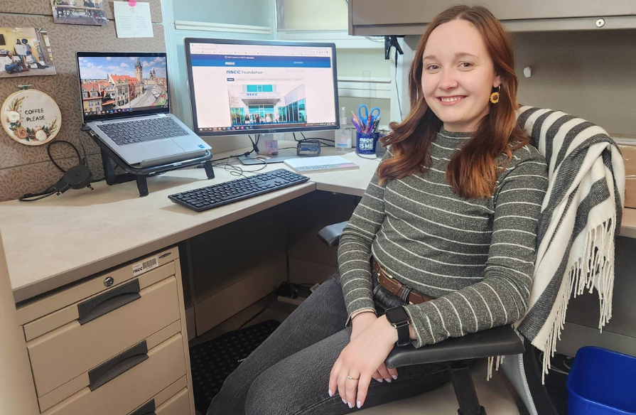Shaylyn MacAulay working in a cubical in the NSCC Foundation and Alumni Relations office, with her laptop opened to the Foundation's website.