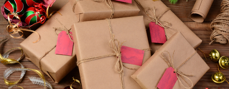 Holiday gifts wrapped in brown paper and string surrounded by festive ribbon.
