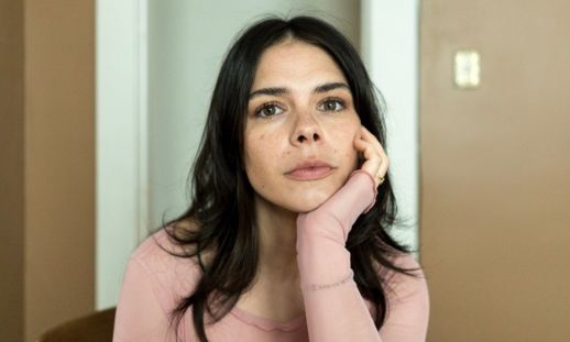 A close-up of a young woman's face. She is seated and resting her head on one hand.