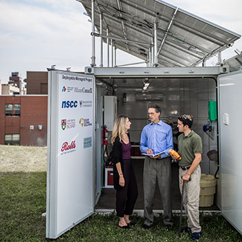 Three research staff, one woman and two men, outside standing in front of the open doors of the deployable microgrid in deep discussion.