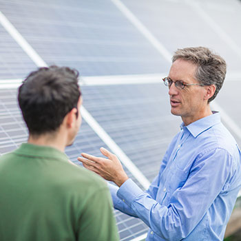 Two males in an animated discussion in front of solar panels.