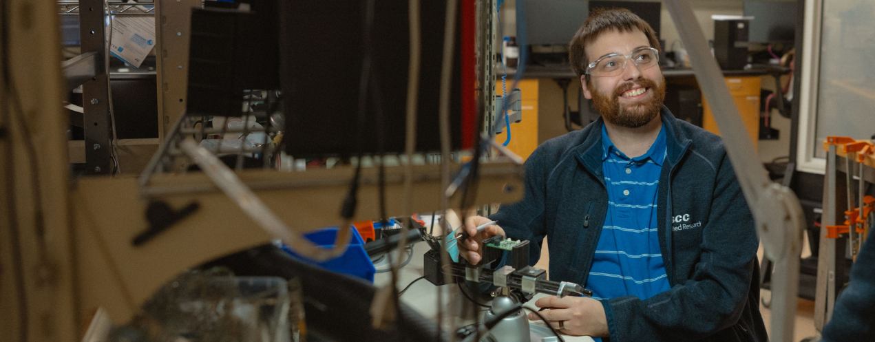 Researcher smiling in a lab surrounded by elect
